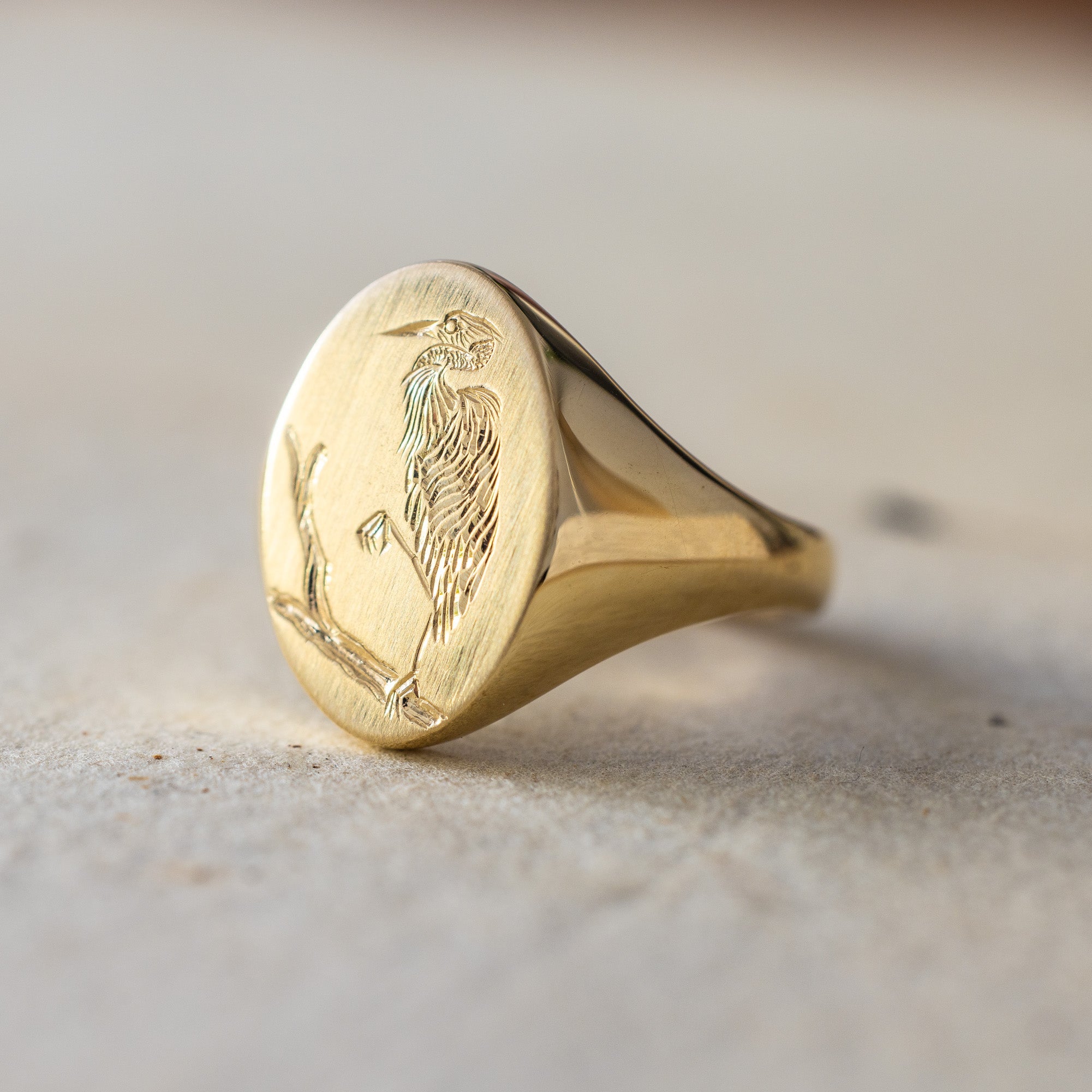 Gold signet ring with engraved design on a beige background